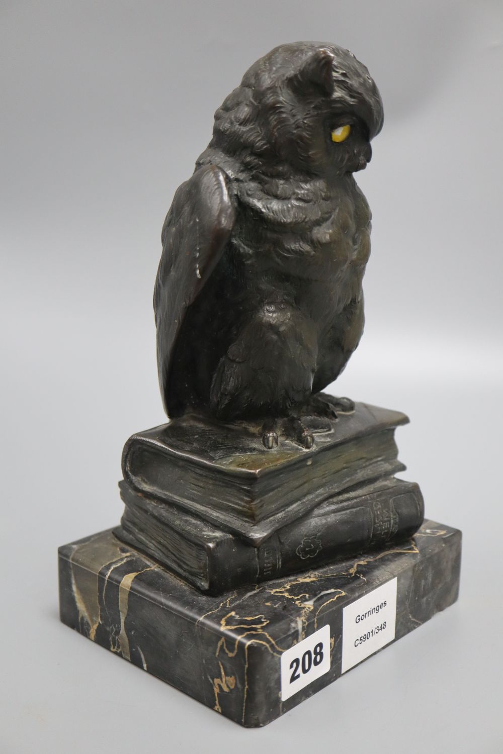 An early 20th century German bronze of an owl, with glass eyes, perched on a stack of two books, on marble base, height 26cm